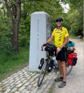Man on bicycle parked in front of the Mason Dixon Line marker