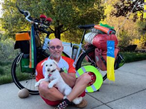 Man holding dog sitting on ground in front of bicycle