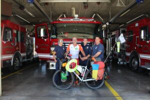 Touring bicyclist standing with his bike in front of fire truck and firefighters