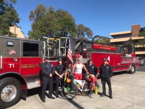Touring bicyclist standing with his bike in front of fire truck and firefighters
