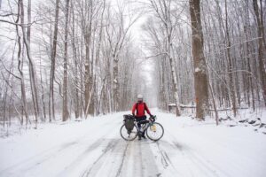 Man riding bicycle on snow covered road through the forest