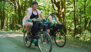 2 ladies bike riding on a trail through the trees