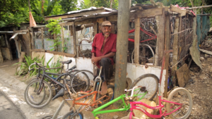 man standing in front of bicycle repair hut with bike parts all around him
