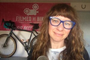 Woman standing in front of a bicycle and banner that says Filmed by Bike