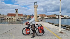 Man on a touring bicycle standing in front of a monument