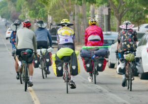 A group of people riding fully packed bicycles down the street taken from the back