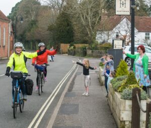 People on the roadside waving to two women riding touring bicycles