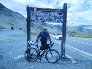 Man posing with a loaded touring bicycle in front of a road sign in Italy.