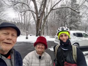 3 people dressed for winter standing on the road, one of them has a touring bicycle