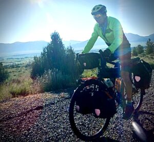 A man riding a loaded touring bicycle on a gravel road