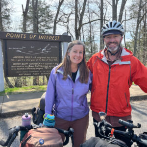 Couple with their loaded touring bicycles posing in front of a points of interest road sign