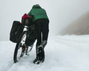 man pushing a loaded touring bicycle through the snow