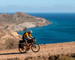 man riding a touring bicycle on a dirt track near the ocean