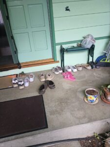 Many pairs of shoes lined up on a house's front porch