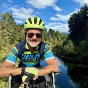 A man on his bicycle wearing a bike helmet on a trail next to a river