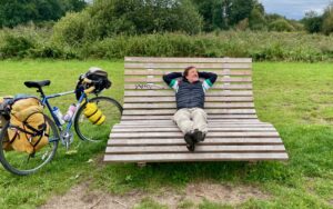 A man reclining on an overly large outdoor chair with his loaded touring bike next to him