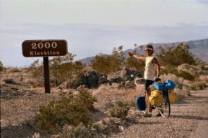 Man on a bicycle pointing to a sign that says 2000 Elevation