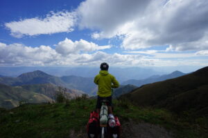 A man standing next to his bicycle looking out at a beautiful mountain view