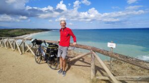 Man with his touring bicycle standing in front of a very blue ocean
