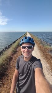 Man with his touring bicycle standing on a very narrow bike trail across a large lake