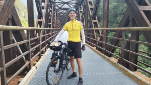 Man with his touring bicycle standing on an iron bridge over a gorge