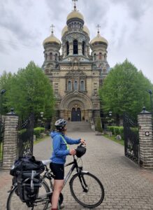 A person standing with their bicycle in front of a cathedral 