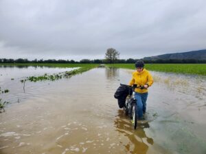 A person walking a bicycle through a flooded field