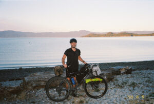 Man standing with a loaded touring bicycle in front of a lake
