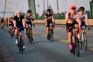 Man riding a bicycle with others across a bridge
