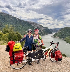 Man and woman with a loaded tandem touring bicycle standing in front of the mountains