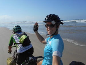 Man and woman riding a loaded tandem touring bicycle on the beach