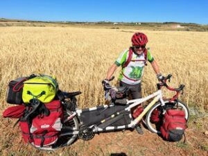 Man with a loaded tandem touring bicycle standing in front of a wheatfield