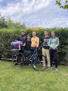 Group of people posing in front of a loaded touring bicycle.
