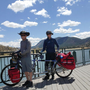 Man and woman on a tandem touring bicycle in front of a lake