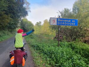 A woman riding a bicycle and pointing to a directional sign that says Dordogne