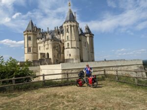 A woman standing with her bicycle in front of a castle.