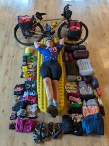 Woman laying on the floor surrounded with her bicycle and all of her touring gear