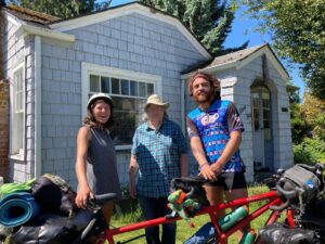 3 people and a tandem bicycle in front of a house