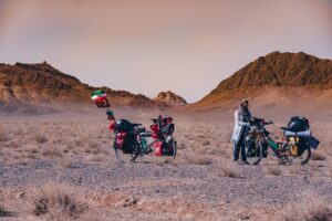 A woman and her touring bicycle in a hilly desert valley