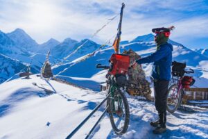 A man and his touring bicycle at the top of a snow covered mountain peak